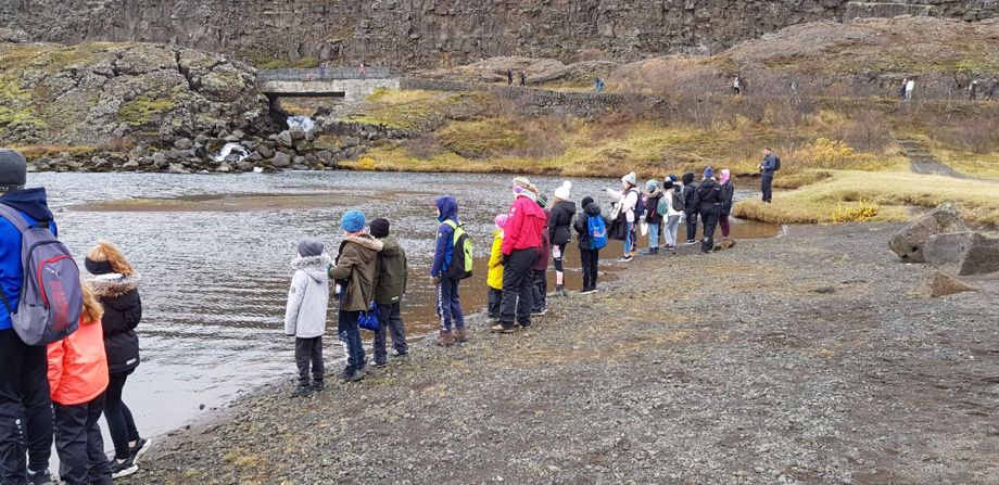 School children stand in a row along the banks of Öxará river at Prestakrókur