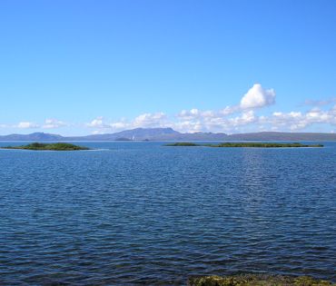 Tveir hólmar út í hinu oft rannsakaða Þingvallavatni á sólríkum degi. Hengill og Grafningur í bakgrunni